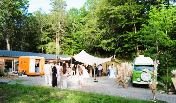 Personnes célébrant un mariage à l'extérieur, entourés de forêt, devant la salle de réception